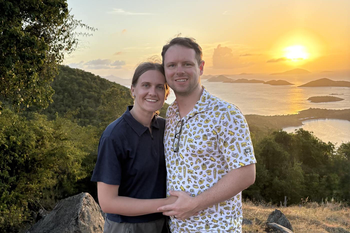 Carter Long and his wife at a hillside overlook on St. John, the sun setting over the water and islands behind them